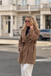 a lady in a brown tencel wool wrap coat and a pair of white pants